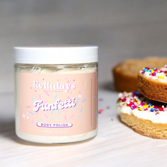 Jar of Kellulays Funfetti Body Polish on a light wooden surface, with colorful sprinkle-covered donuts in the background, reflecting a playful and festive theme.