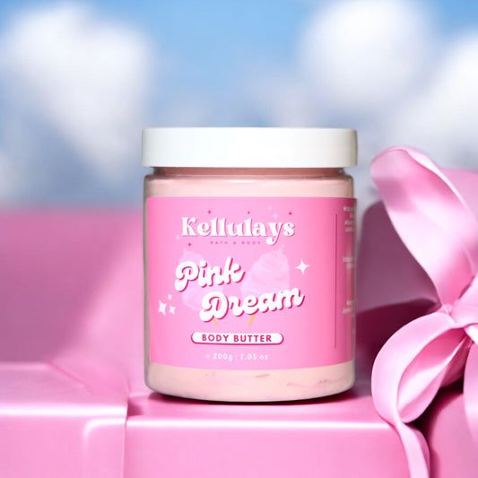 Kellulays Pink Dream Body Butter: A 200g jar of body butter with a pink label adorned with whimsical stars and clouds, placed against a pink gift box tied with a satin ribbon. The background features a soft blue sky with fluffy white clouds, creating a dreamy and playful aesthetic.