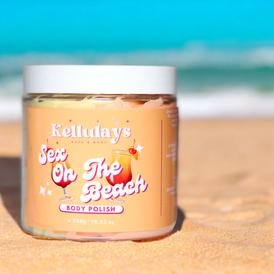 Jar of Kellulays ‘Sex On The Beach’ body polish on a sandy beach with ocean background, featuring a peach label with tropical cocktail illustrations.