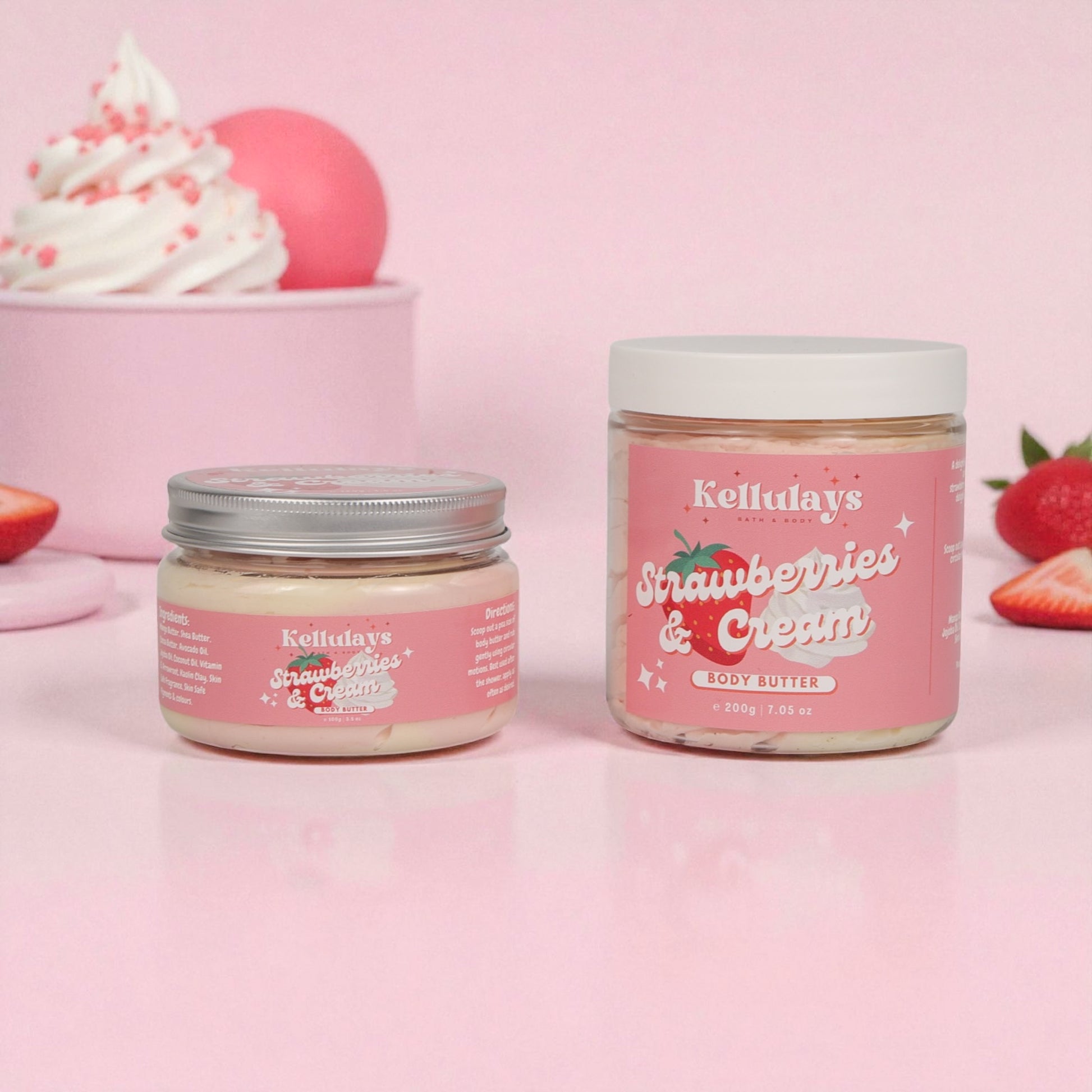 Two jars of Kellulay's Strawberries & Cream body butter on a pink background with strawberries and whipped cream.