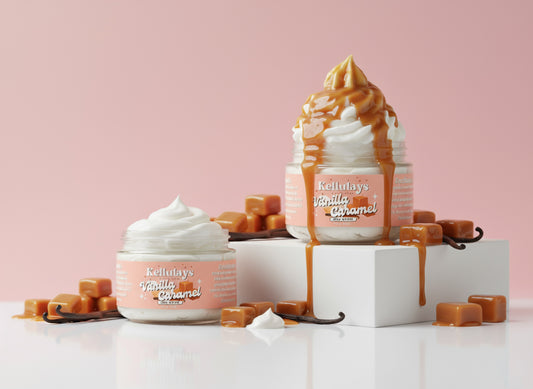 Two jars of Kellulays Vanilla Caramel whipped body butter styled against a soft pink background. One jar features a smooth white swirl, while the other is topped with a tall whipped peak covered in dripping caramel sauce. Caramel cubes and vanilla beans surround the jars for dessert inspired skincare aesthetic